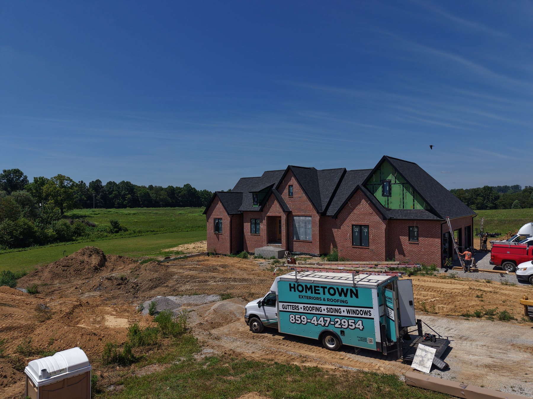 Brick new-construction home in progress with ZIP on gables and Hometown Exteriors and Roofing truck on site