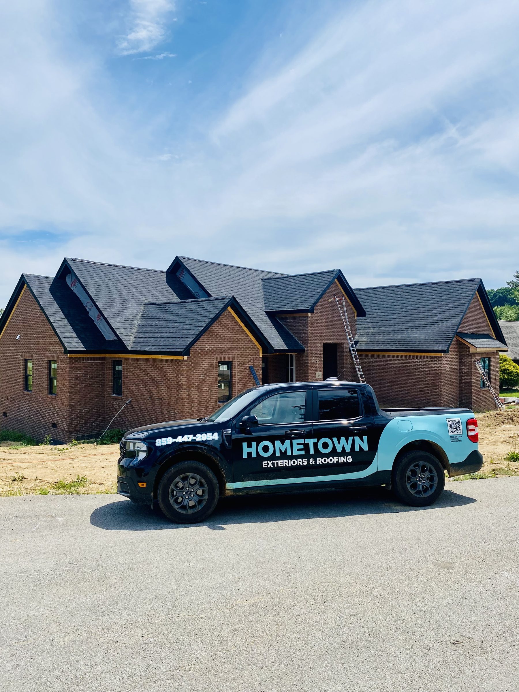 Hometown Exteriors and Roofing branded teal fleet truck with phone 859-447-2954 at a brick residential roofing project