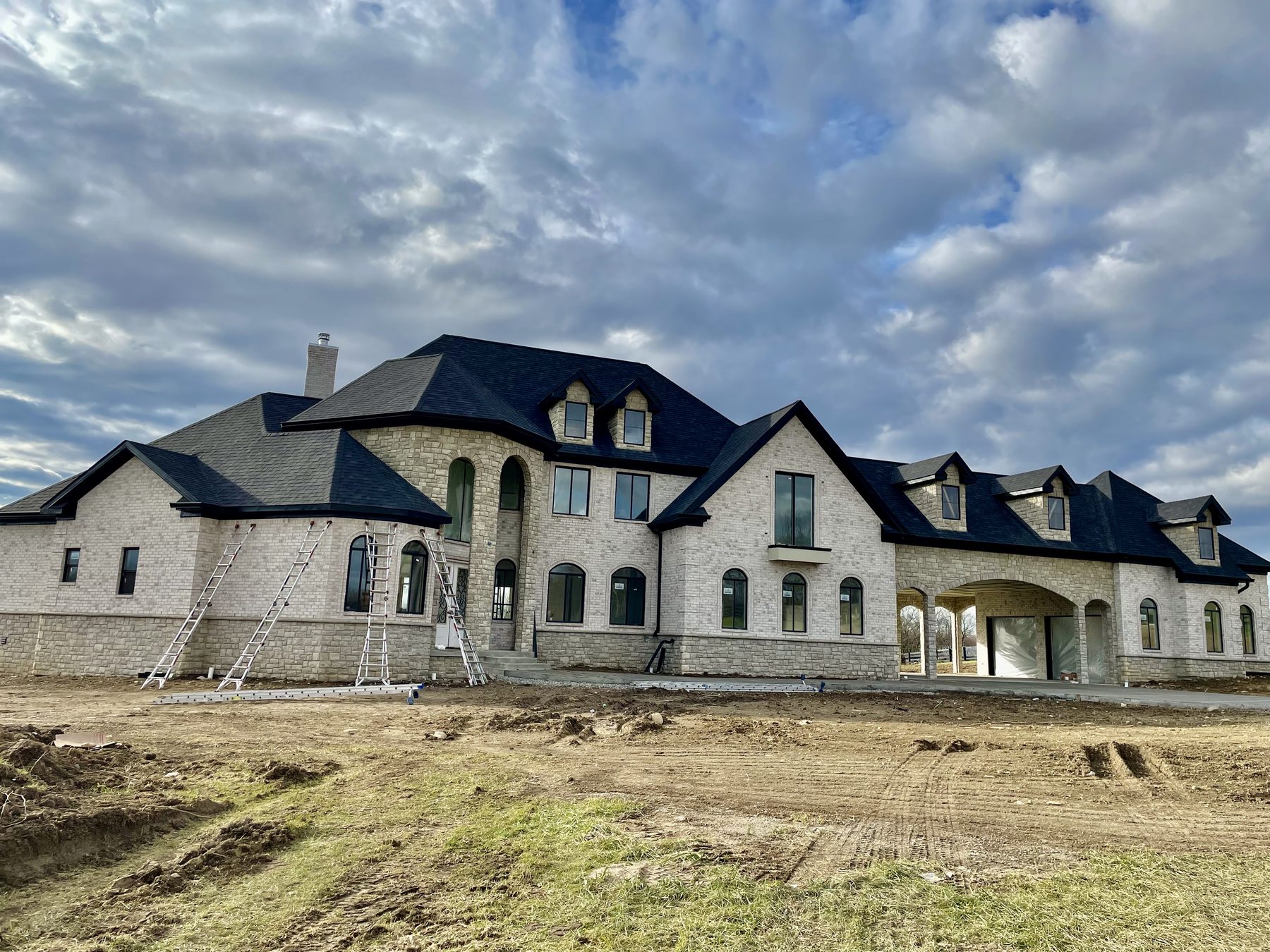 Light-stone luxury new-construction home with dark charcoal multi-gable roof and ladders on site by Hometown Exteriors and Roofing